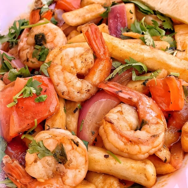 Close-up of Peruvian Lomo Saltado with shrimp, fries, red onions, tomatoes, and cilantro.