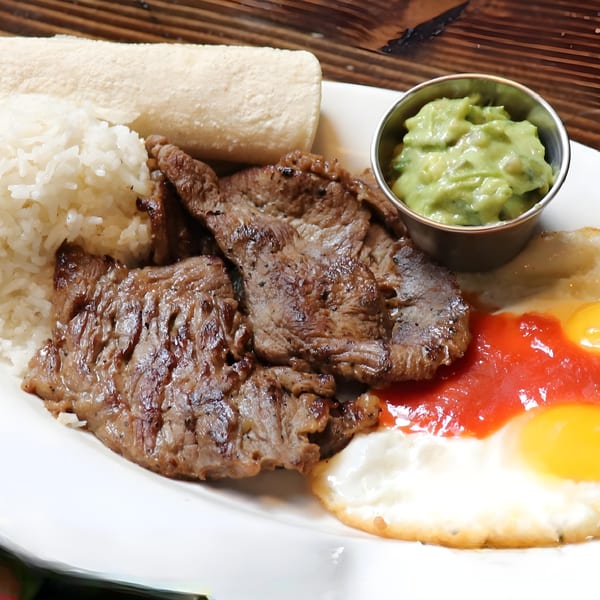 Peruvian grilled steak with rice, fried eggs, red sauce, guacamole, and a white flatbread.