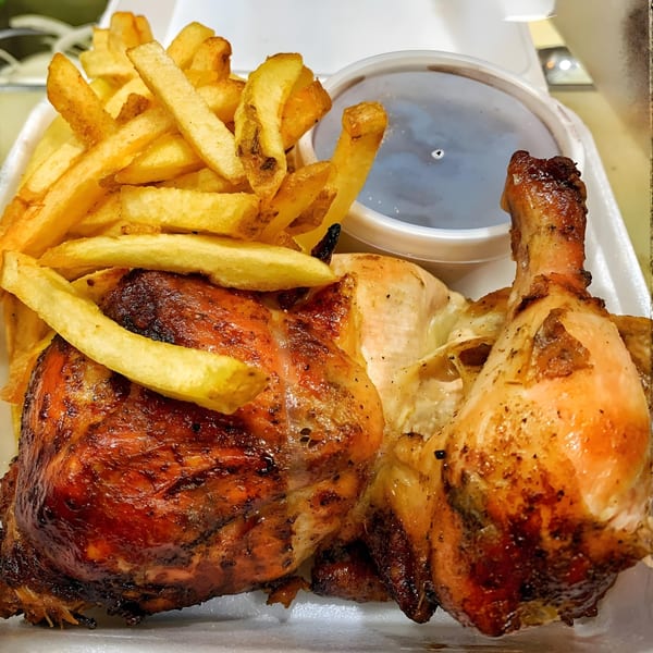 Peruvian rotisserie chicken with crispy skin, a pile of golden french fries, and a side of dark sauce.